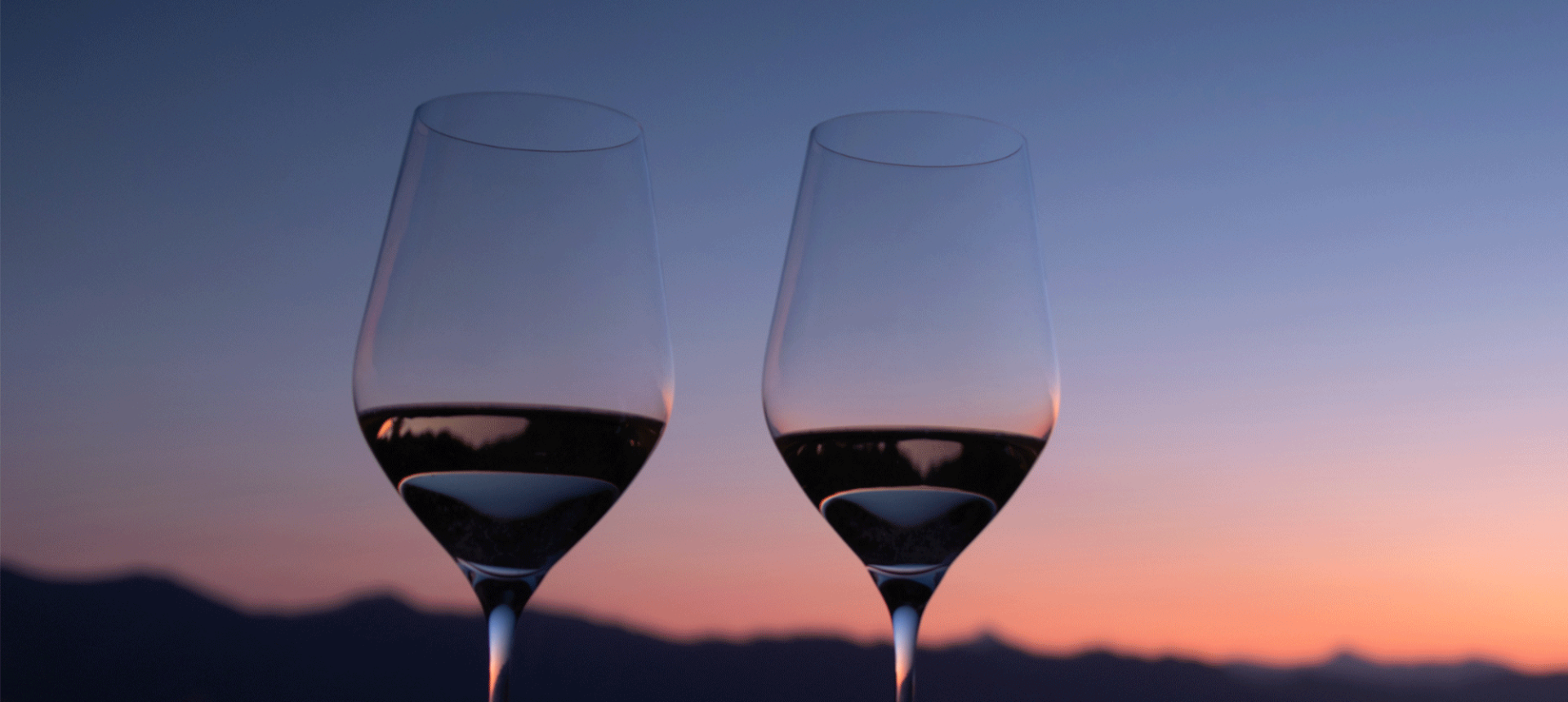 two glasses sitting on a table with the sun setting in the back ground