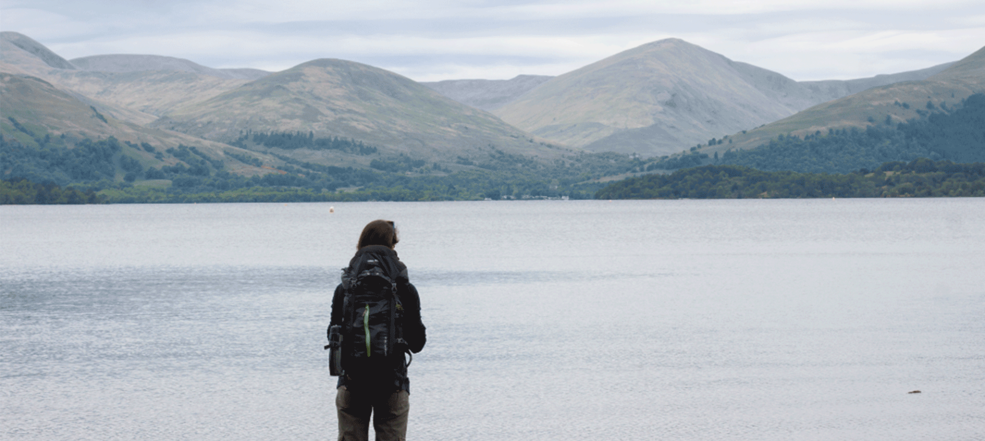 a person standing on the side of the water looking out at the mountains in the back ground