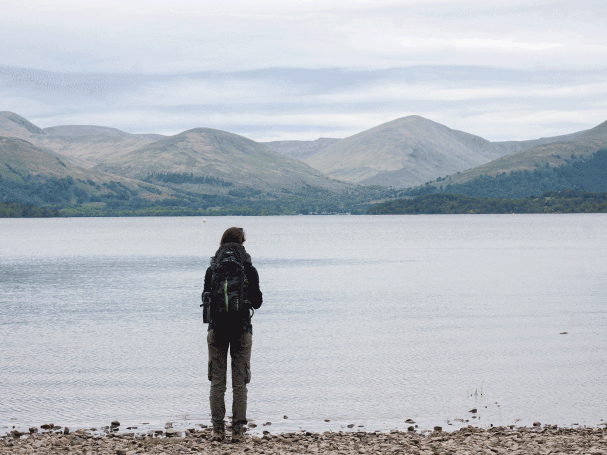 a person standing on the side of the water looking out at the mountains in the back ground