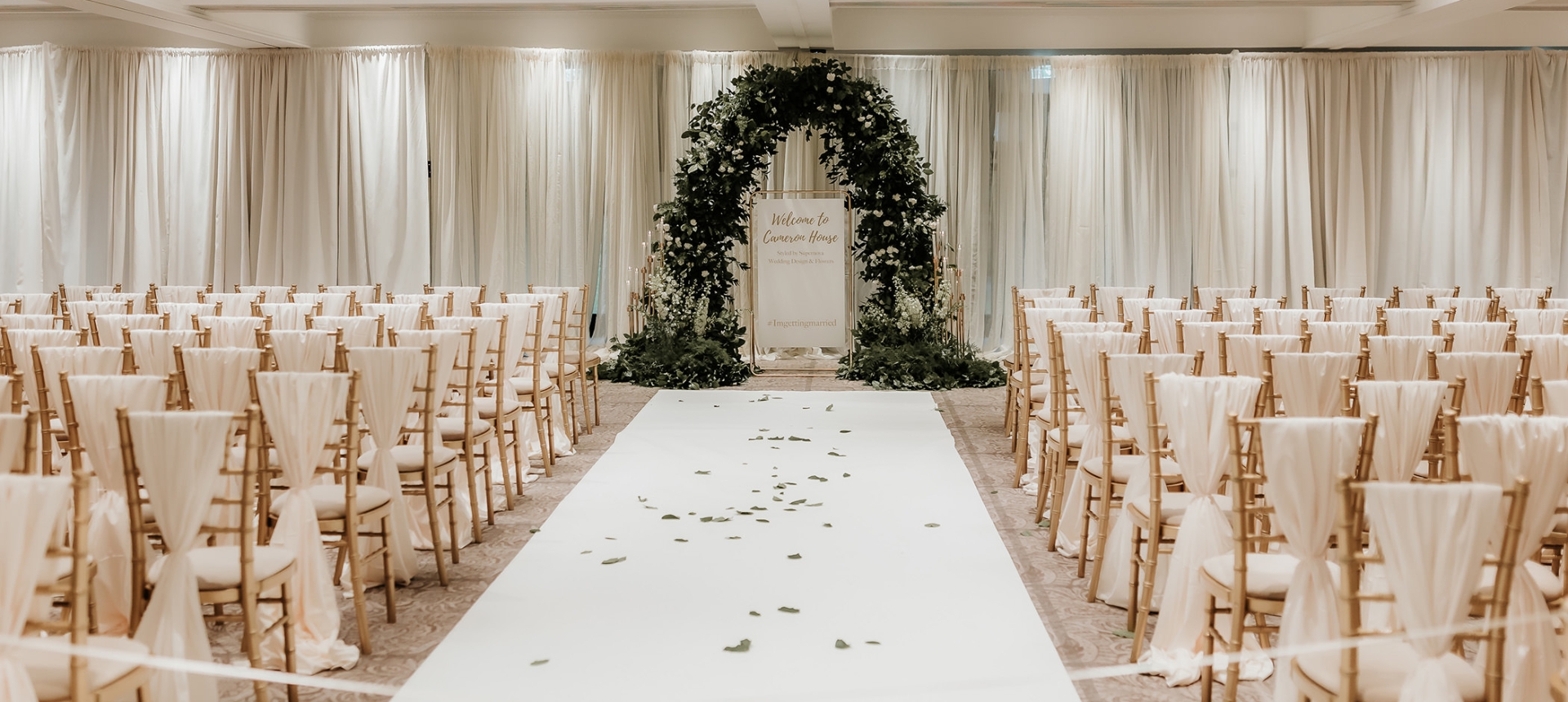 large wedding area with flower arch and white carpet leading up to it