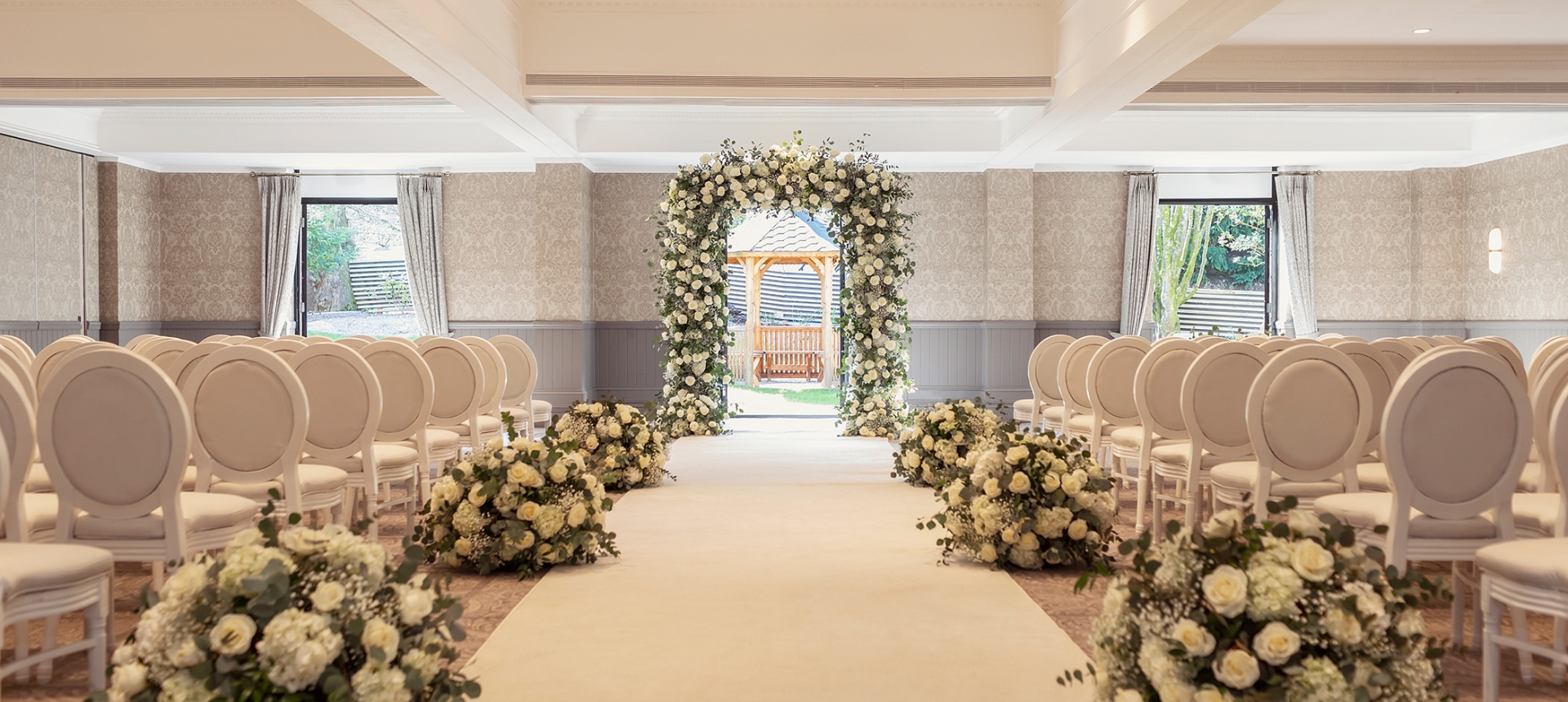 a walking space with a white carpet and flower bushes on each side leading to a outdoor gazebo