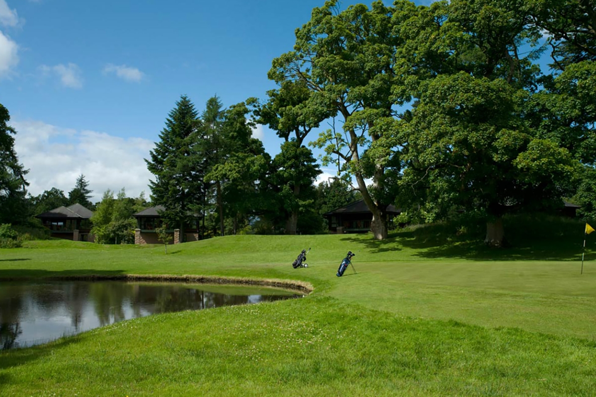 a golf course with two bags set up by the hole on the edge of a lake