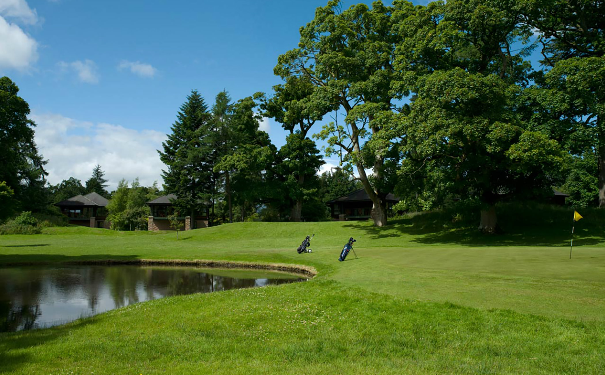 a golf course with two bags set up by the hole on the edge of a lake