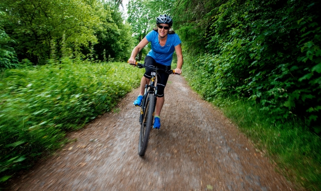 a woman riding her bike down a trail with trees and bushes around her
