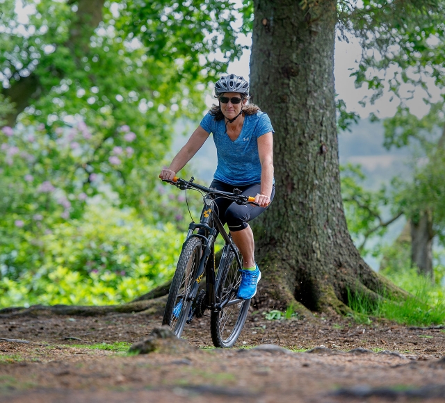 a woman riding her bike in the forest with a tree in the background