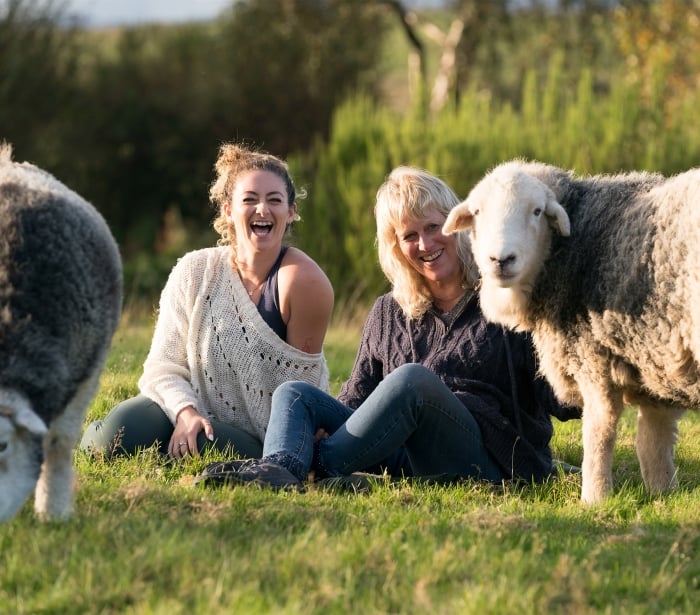 two woman sitting in the grass petting sheep