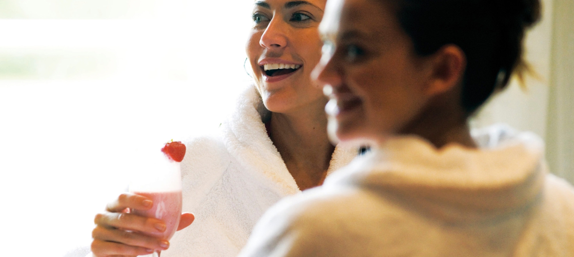 two woman in robes enjoying themselves with one of them holding a drink