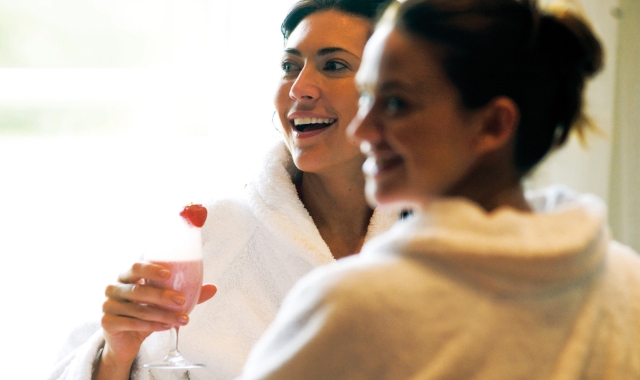 two woman in robes enjoying themselves with one of them holding a drink