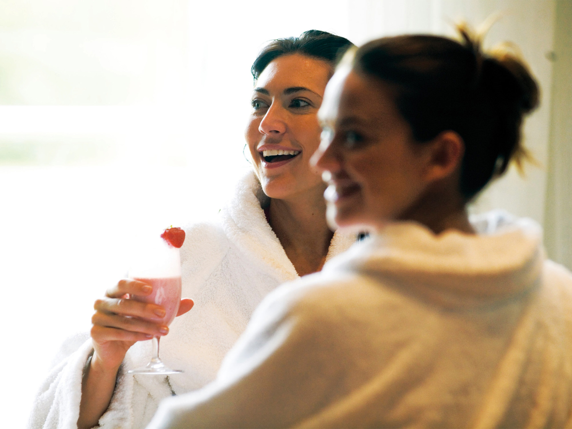 two woman in robes enjoying themselves with one of them holding a drink