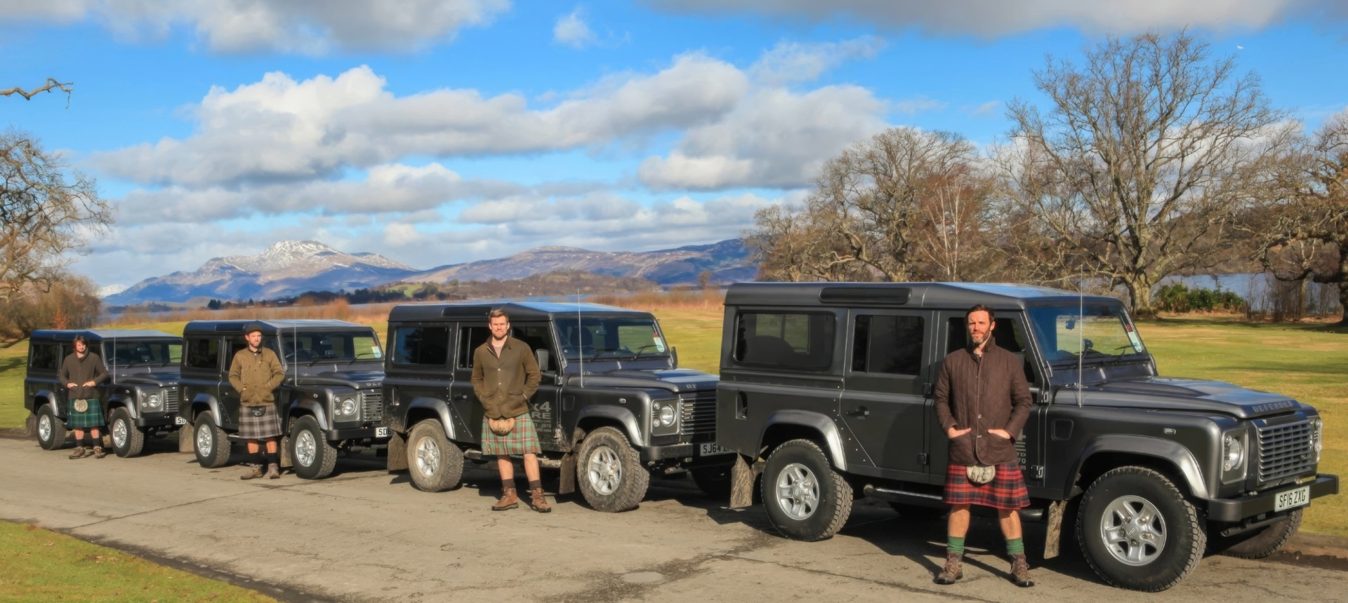 a group of 4 men standing in front of 4 black SUVs