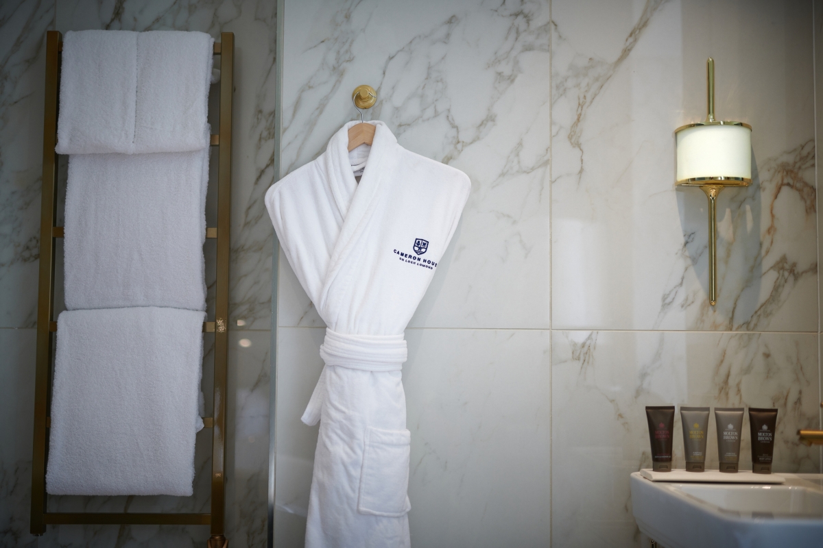 A Cameron House branded bathrobe, fluffy white towels and bathroom products on a sink