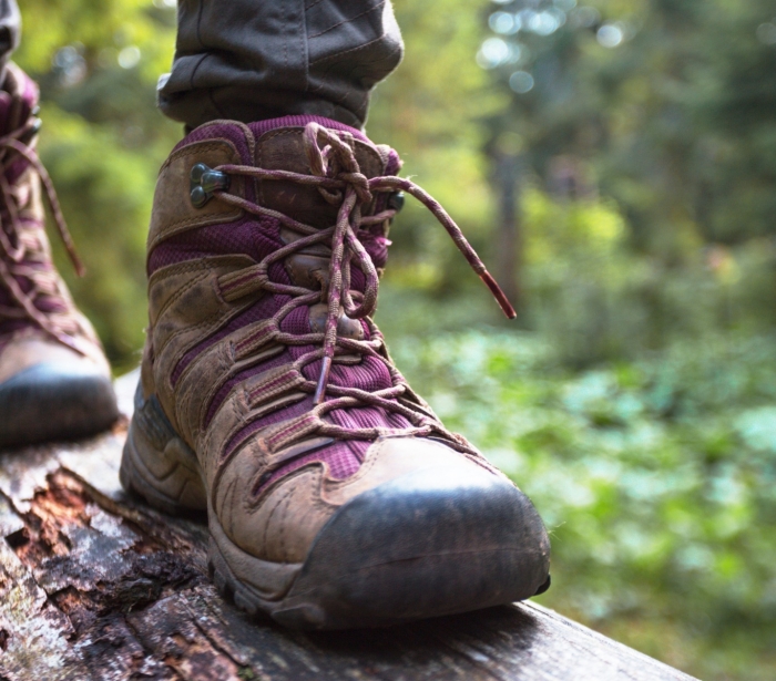 A person wearing hiking boots walking across a log