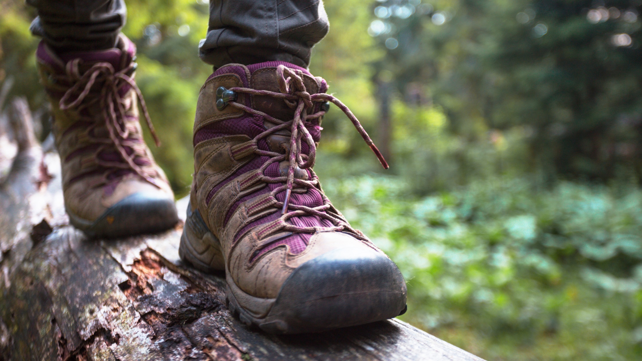 A person wearing hiking boots walking across a log
