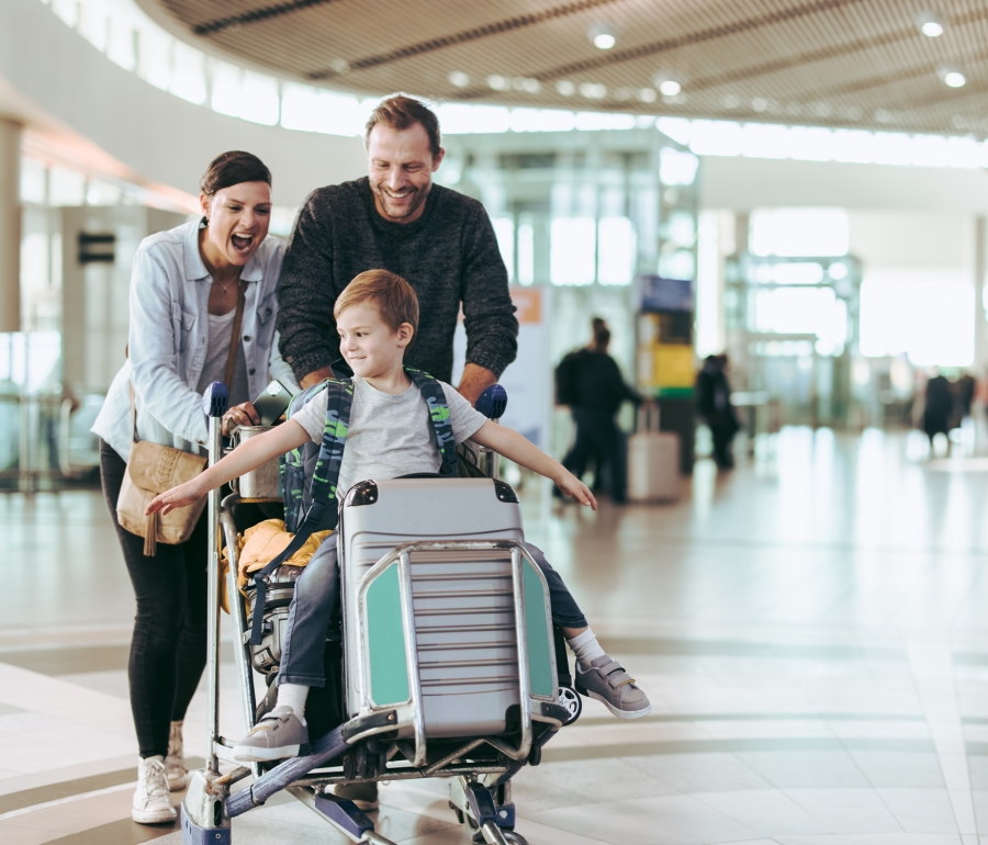 A family with a child riding luggage and navigating an airport.